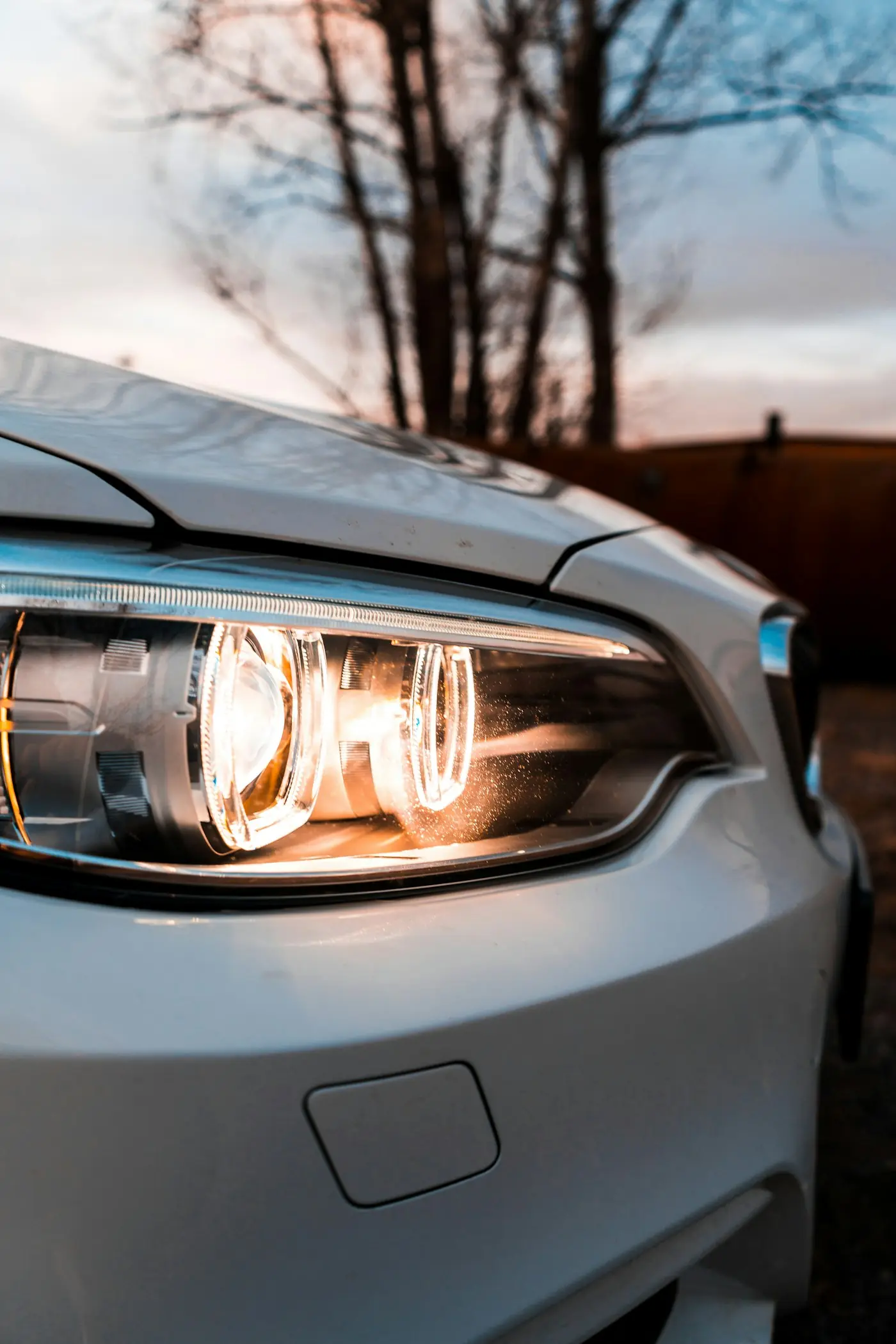 Lit headlight on a white car at dusk